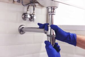 Plumber repairs and maintains chrome siphon under the washbasin.