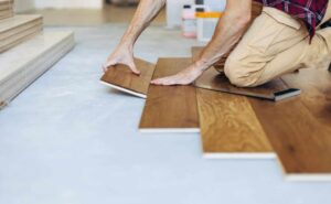 The man is installing the wooden plank of the parquet floor in his home