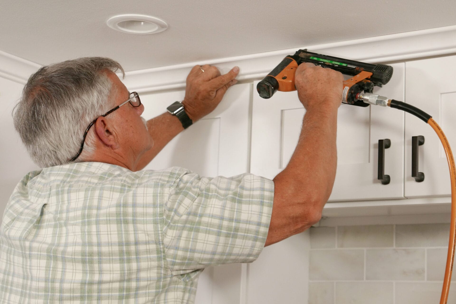 Tom Silva installing crown molding above a kitchen Cabinet.