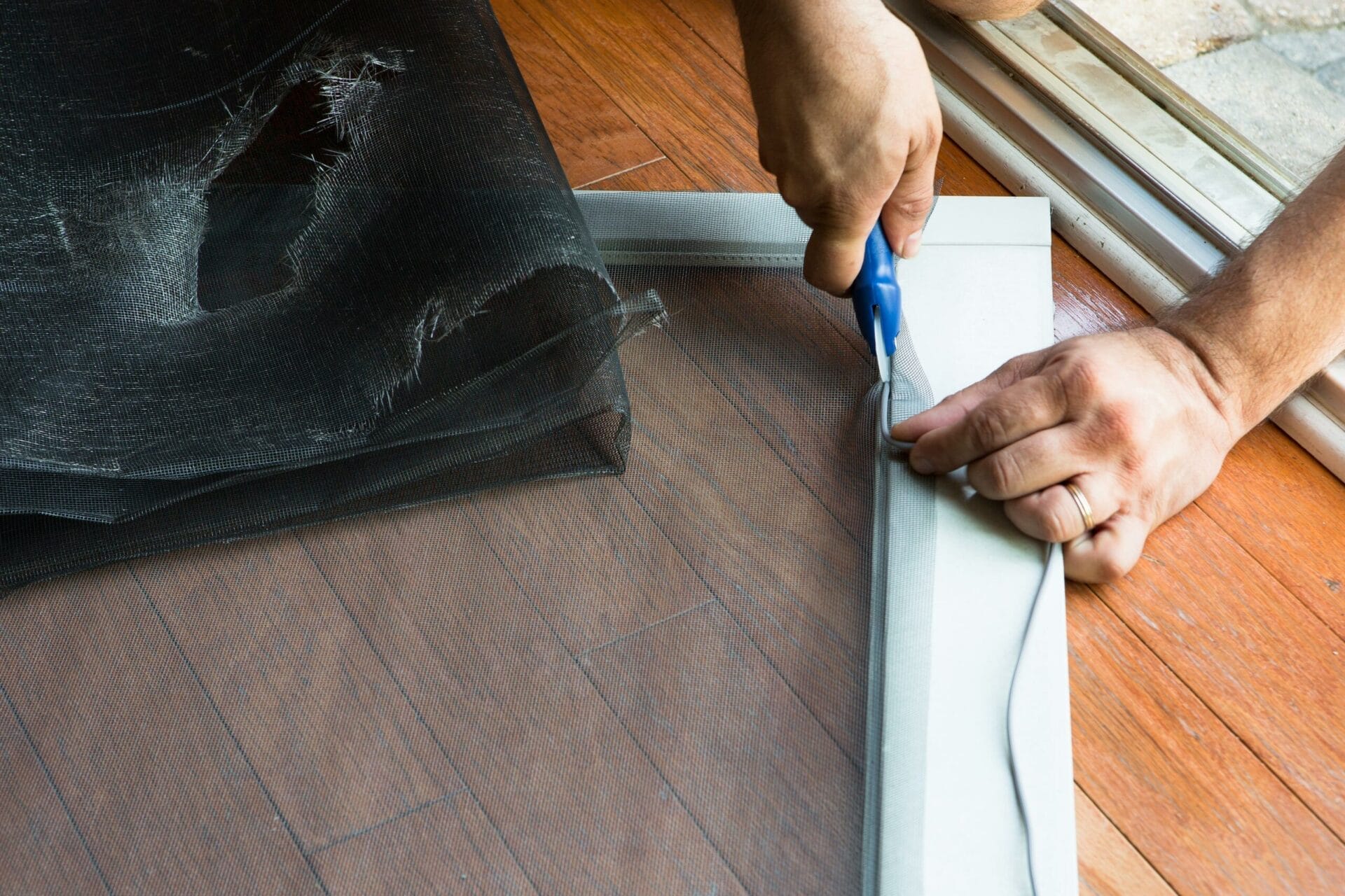 Person cutting a screen to size to replace a ripped screen door.